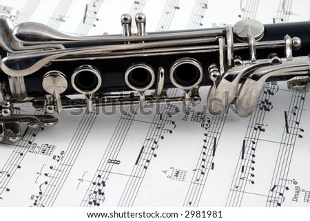 Middle of a clarinet with holes and keys lying on some sheet music