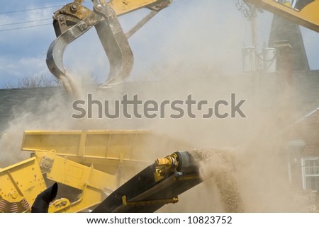 Yellow construction equipment loading rubble into a dump truck  (a lot of construction dust showing)