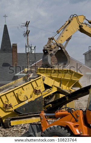 Construction site with rubble being put into a dump truck with a bulldozer in the foreground