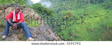 African man in the tropical jungle with waterfall fog in the background - Cameroon - Africa - Panorama.