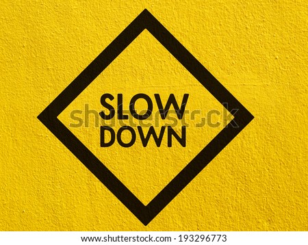 Slow Down yellow road sign painted on a stucco wall outside