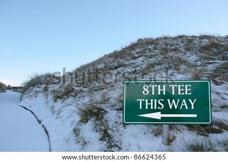 8th tee this way sign on a snow covered links golf course in ireland in snowy winter weather
