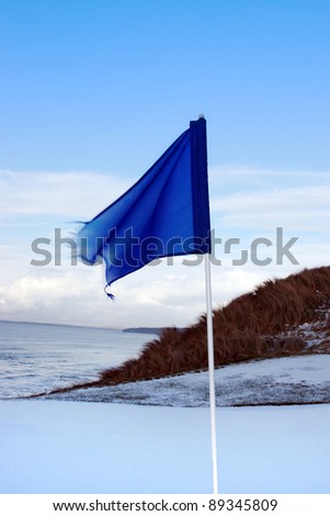 a snow covered links golf hole in ireland in winter weather with blue flag