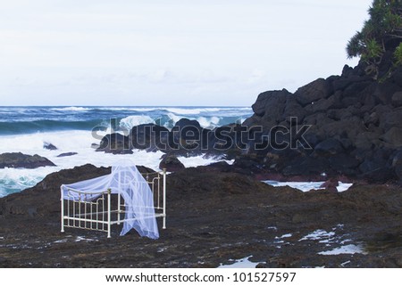 Iron bed frame and mosquito net on beach rocks