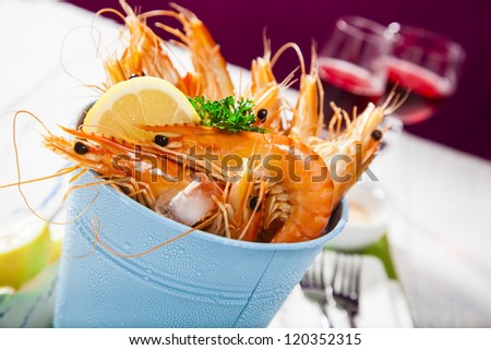 Bucket of king prawns on ice with lemon, sauce and two glasses of wine