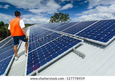 Young technician inspecting solar panels on factory roof