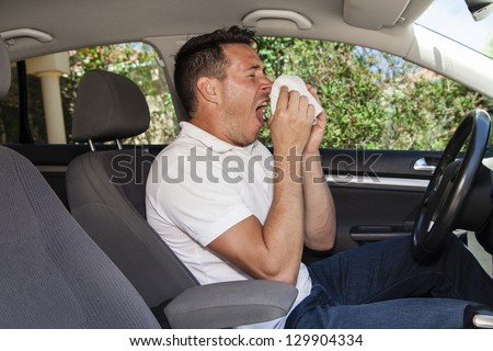 Man allergic to pollution or pollen sneezing inside a car.