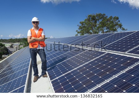 Young technician standing with solar panels on factory roof