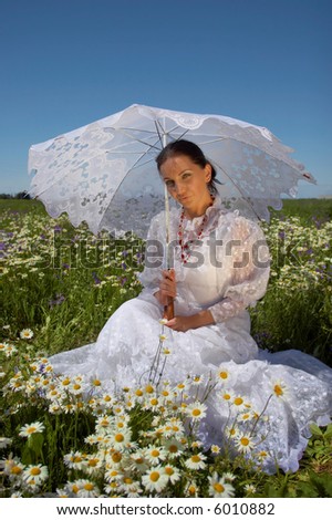 Beautiful young woman, in a white dress under a white umbrella with camomiles, in a field