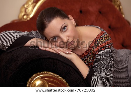 Portrait of an elegantly beautiful young woman posing on an antique sofa