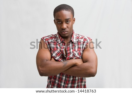 Young dark skinned handsome guy standing like a macho with both arms crossed wearing a checkered shirt without sleeves.