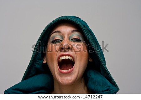 A beautiful young woman screaming aggressively wearing a green winter coat and the hood over her head