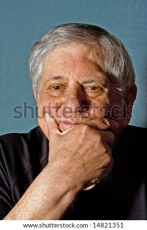 Dramatic portrait of a senior man with his hand on his chin wearing a black shirt isolated on gray/blue