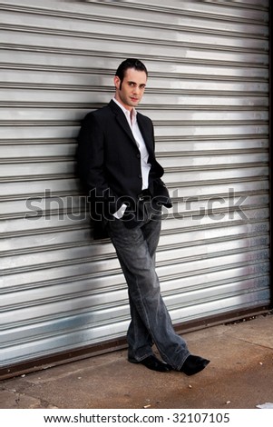 Handsome casual business man standing in front of and leaning against silver metal garage door with hands in pocket