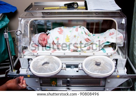 Cute sick newborn premature neonatal baby swaddled in bunny blanket placed in incubator chamber in hospital.