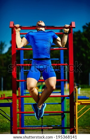 Handsome healthy happy srtong athlete male man exercising at the city park - fitness concepts on a beautiful summer day on horizontal bar