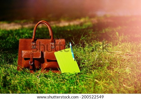 Retro brown  man leather bag and notebook in bright colorful summer grass in the park