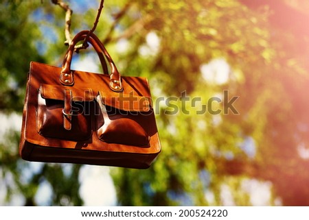 Retro brown  man leather bag  in bright colorful summer park hanging on leaves