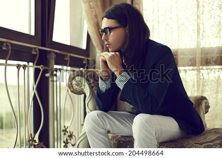 portrait of sexy attractive stylish model man with long hair in costume sitting on the sofa in classic interior