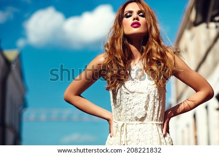 High fashion look.glamor beautiful sexy stylish blond young woman model with bright makeup and pink lips with perfect clean skin in white summer dress in the city behind blue sky