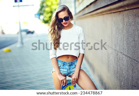 portrait of sexy young stylish smiling woman girl  model in bright modern cloth in glasses outdoors in the street in jean shorts with skateboard