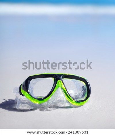 green snorkel and waterproof mask lying on sand behind blue sky and ocean
