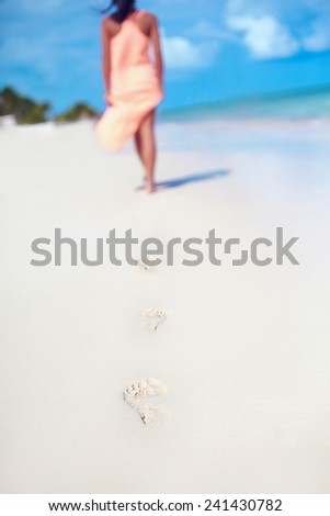 woman in colorful dress walking on beach ocean leaving footprints in the sand