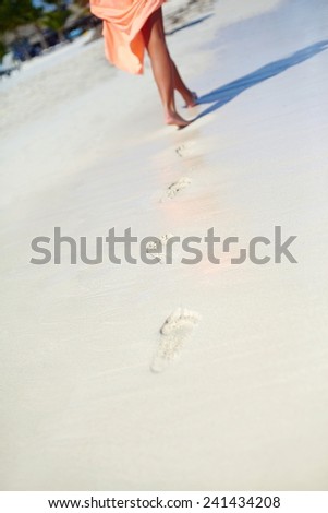 woman in colorful dress walking on beach ocean leaving footprints in the sand