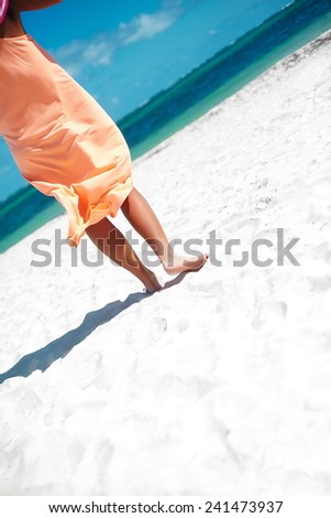 Hot beautiful woman in dress walking near beach ocean on hot summer day on white sand