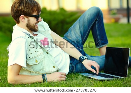 Funny smiling hipster handsome man guy in stylish summer cloth in grass with notebook