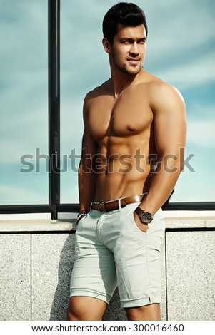 Fashion portrait of young sexy  handsome muscled model man in casual cloth  in sunglasses in the street showing his  abdominal muscles