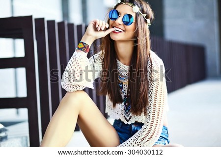 Funny stylish sexy smiling beautiful young hippie woman model in summer white fresh hipster clothes sitting in the street
