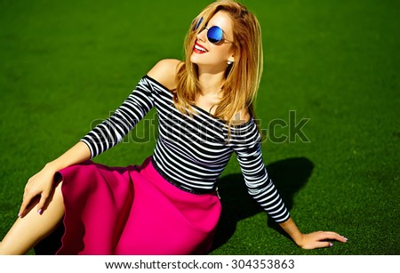 Funny crazy glamor stylish sexy smiling beautiful blond young woman model in pink hipster clothes sitting in the grass in the park