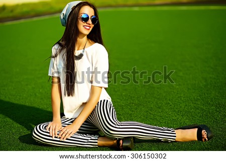 Funny crazy glamor stylish sexy smiling beautiful  young woman model in hipster clothes in beanie sitting in the grass in the park