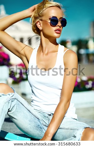 High fashion look.glamor stylish beautiful young blond  model girl teenager in summer bright casual hipster clothes with skateboard behind blue sky in the street