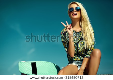 High fashion look.glamor stylish sexy beautiful young blond  model girl in summer bright casual hipster clothes with skateboard behind blue sky