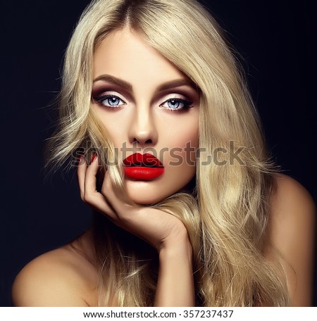sensual glamour portrait of beautiful blond woman model lady with bright makeup and red lips touching her face , with healthy curly hair on black background