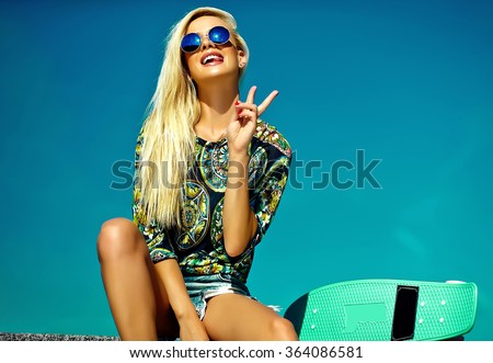 High fashion look.glamor stylish sexy beautiful young cute blond model girl in summer bright casual hipster clothes with skateboard behind blue sky showing victory sign