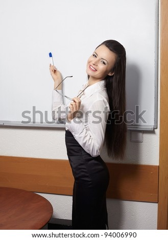 young smiling businesswoman standing near board and pointing at the board in glasses in the office