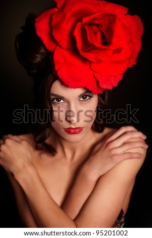 fashion portrait of beautiful woman with bright makeup and red lips with big red rose on head on black background
