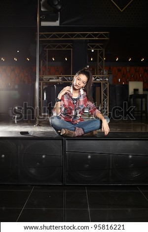 young beautiful smiling pop star singer with microphone sitting on the scene in the club