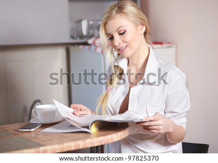 Beautiful young woman holds sitting in the kitchen and read magazine