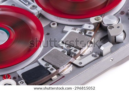 Medium close shot of a reel to reel audio tape recorder with spinning reels on white background