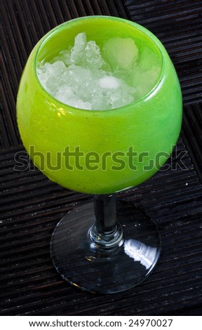 A frozen margarita in a decorative glass on a hardwood surface.