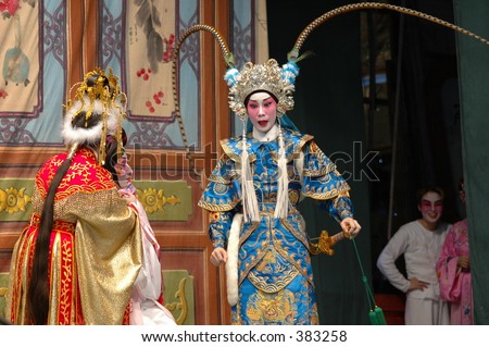 Chinese opera performers on stage in full makeup and costume  with understudies in the wings watching