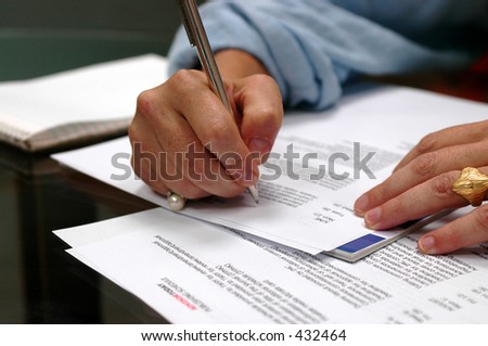 close-up shot of a business woman\'s hands writing or taking notes amidst papers and reports