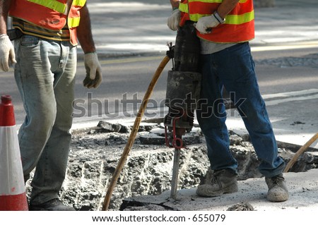 Road workers on a sidewalk with a jackhammer digging up concrete