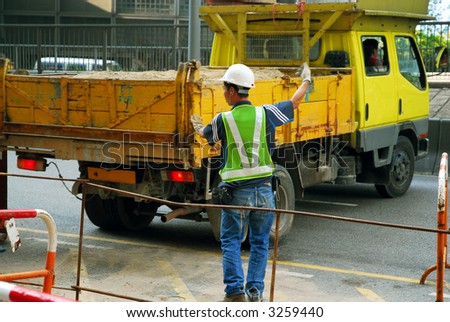 Worker directing a sand-filled dump truck at a construction site