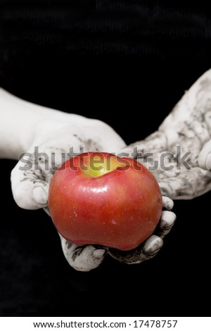 a bright red apple in muddy, dirty hands in black and white