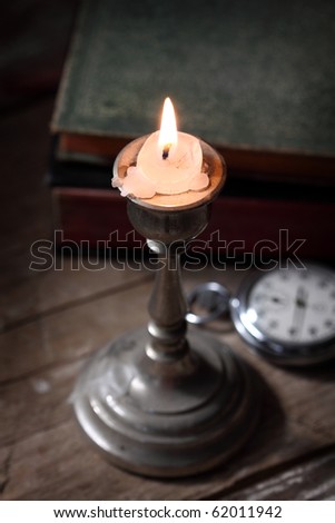 glowing candle on a table, clock and books